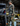 Man in camouflage gear with a bow and arrow standing next to a vehicle in a warehouse.